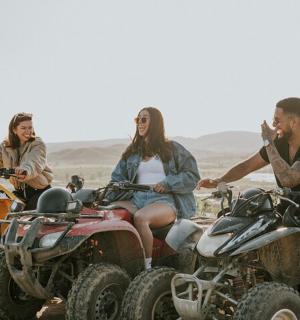 三个人坐在沙漠中的四轮摩托车上