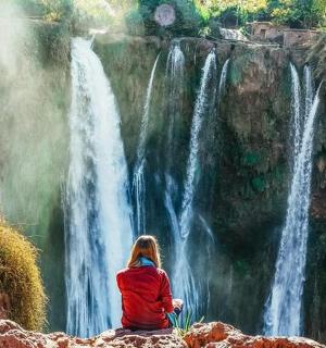 一位女士坐在瀑布前的岩石上