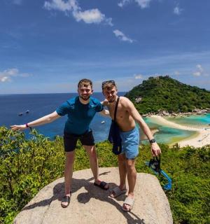 two men standing on top of a rock near the ocean