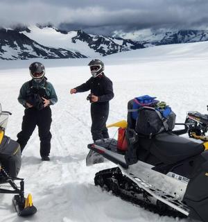 three men standing in the snow next to a snowmobile