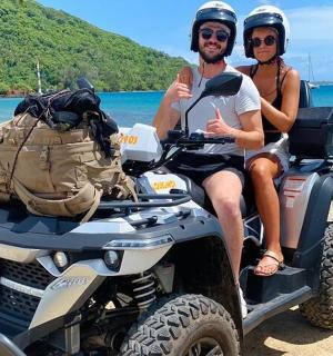 两个人坐在沙滩上的一辆四轮摩托车上