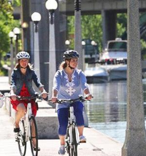 three women riding bikes down a sidewalk next to a river