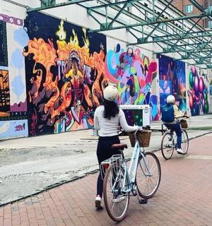two people riding bikes in front of a wall with graffiti