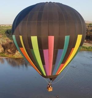 Barevný horkovzdušný balón letící nad řekou