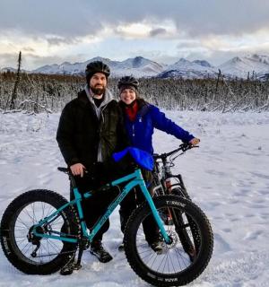a man and woman posing with a bike in the snow