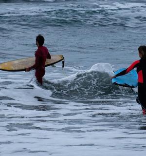 two people walking into the ocean with surfboards