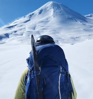 muž s batohem a lyžemi na zasněžené hoře