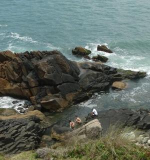 two people sitting on the rocks near the ocean