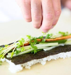 a person sprinkling vegetables on top of a sandwich