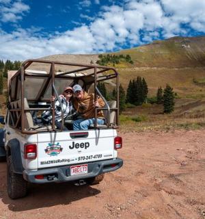 dva lidé sedící v zadní části nákladního auta na nezpevněné cestě