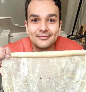 a man is holding up a piece of dough