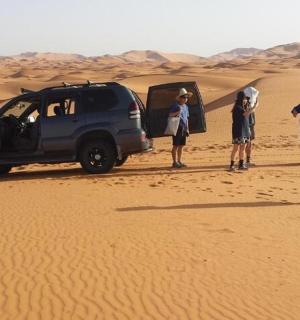 a group of people standing next to a vehicle in the desert