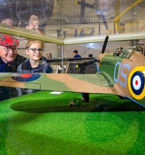 two men standing next to a small green airplane