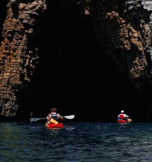 two people in kayaks in the water near a cave