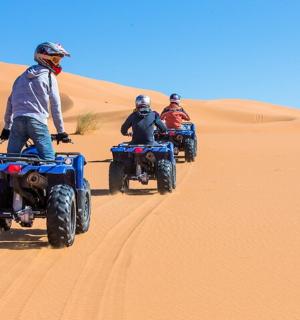 trije ljudje se vozijo na štirikolesnikih v puščavi