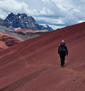 a man walking down a dirt hill with mountains in the background