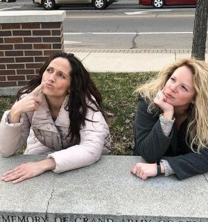 two women laying on the grass with their fingers in their mouths