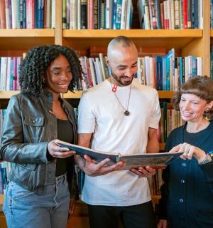 drie mensen staan in een bibliotheek en kijken naar een boek