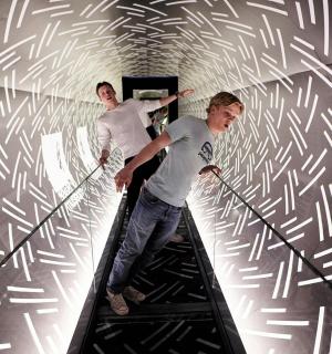 两名男子在隧道的自动扶梯上行走,隧道的墙壁上有图案