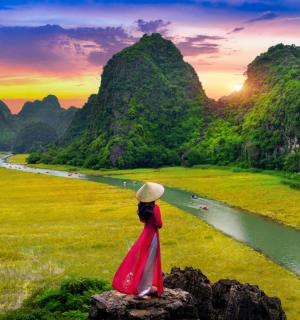 一位身穿红裙的女子站在岩石上，俯瞰着一条河流