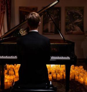 一名男子坐在钢琴前，点着蜡烛