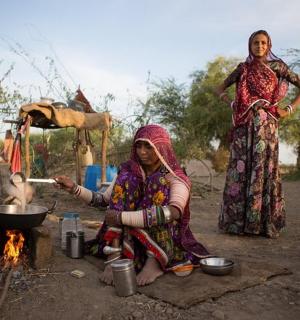two women standing next to a fire with a pot