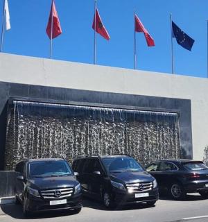 tři auta zaparkovaná před budovou s vlajkami