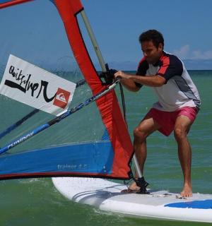 un home sobre una taula de surf amb una vela a l'oceà