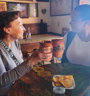 一位女士坐在桌边,另一位女士手里拿着饮料