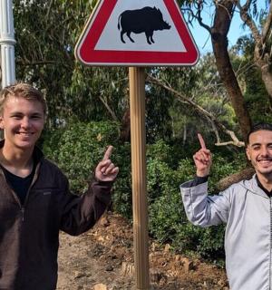 两名男子站在一块牌子旁边,牌子上有一头牛