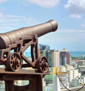 a statue of a cannon with a city in the background