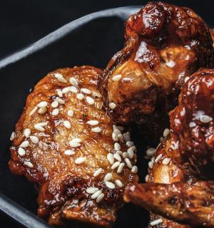 a black plate of food with chicken with sesame seeds