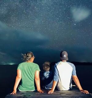 a group of three people sitting on a dock looking at the stars