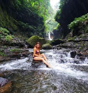 一位女士坐在瀑布边的一块岩石上