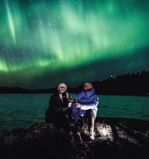 two people sitting on a rock under the northern lights