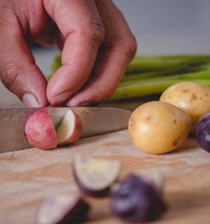 a person cutting up potatoes on a cutting board with vegetables
