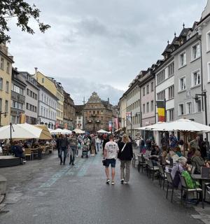 a group of people walking down a street with tables and chairs