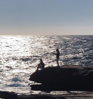 two people standing on a rock in the ocean