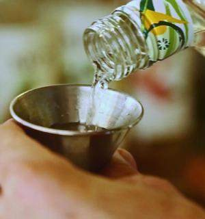 osoba držící hrnek pod lahví s vodou