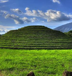 一片广阔的绿色田野,中间有一座长满草的小山。