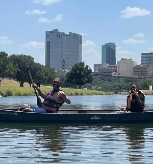 two people in a canoe on the water with a city in the background