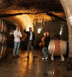 Skupina lidí stojících ve vinném sklepě se sudy