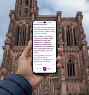 asmuo, laikantis mobilųjį telefoną priešais pastatą