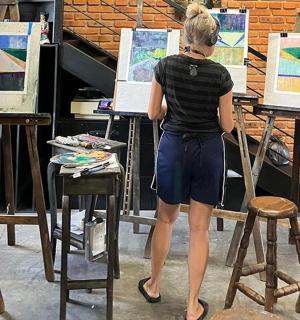 一位女子站在凳子上,面前是几幅画作。