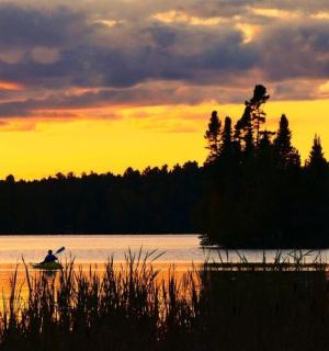 eine Person in einem Boot im Wasser bei Sonnenuntergang