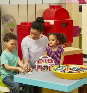 ein Mann und zwei Kinder spielen mit einem Spielzeughaus