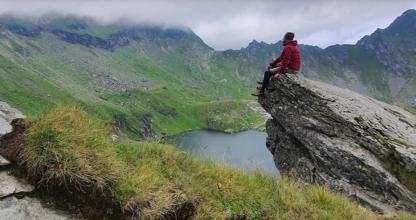 a man sitting on top of a mountain overlooking a lake