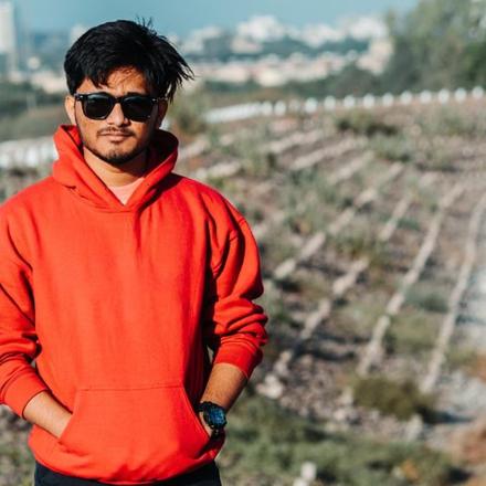 a man in an orange sweater standing in front of a vineyard