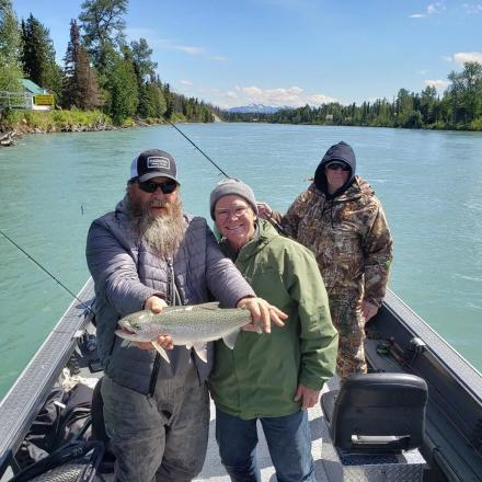 three men in a boat holding a fish on a river