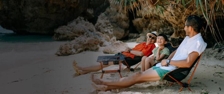 A family of three, sitting on the beach and laughing